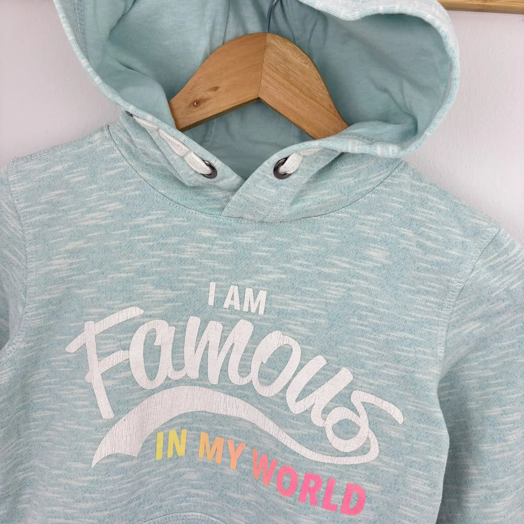I am Famous in My World felirat a világoskék pulóveren közelről