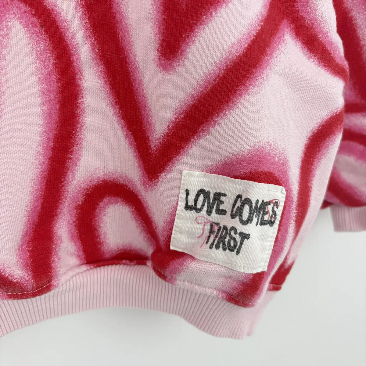Love Comes First felirat a rózsaszín pulóveren közelről